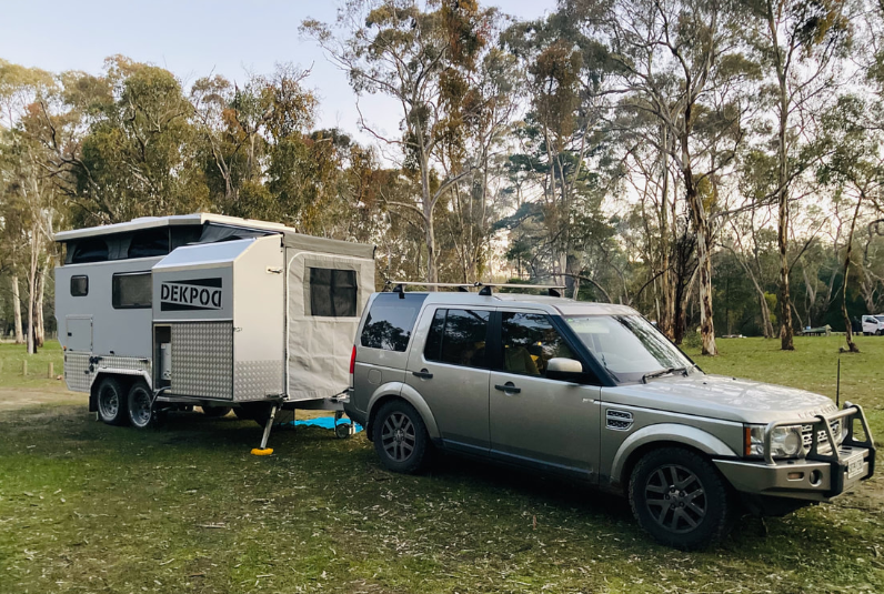 A vehicle on a grass field, surrounded by gum trees, with the HUTrv DEKPOD prototype attached.